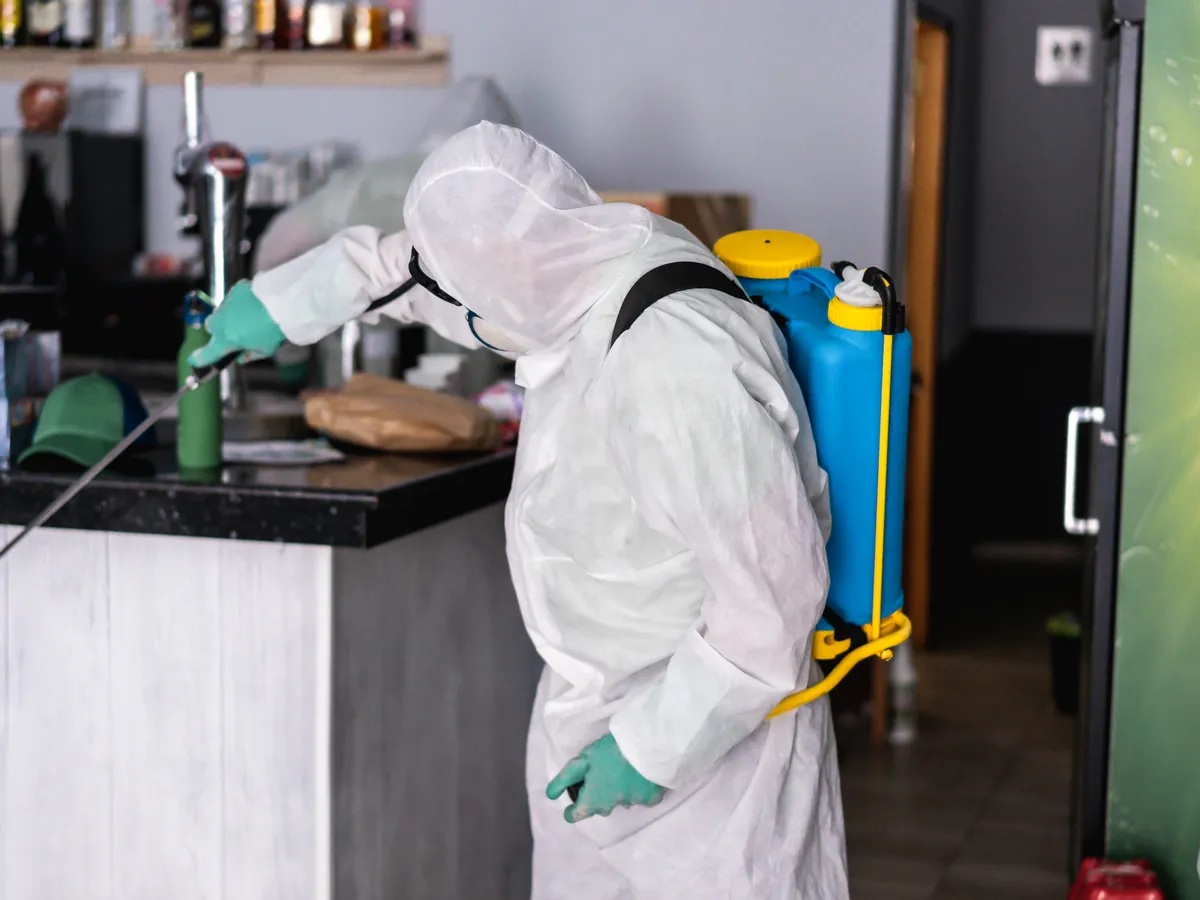 Technicien en combinaison de protection qui traite le comptoir d’un restaurant
