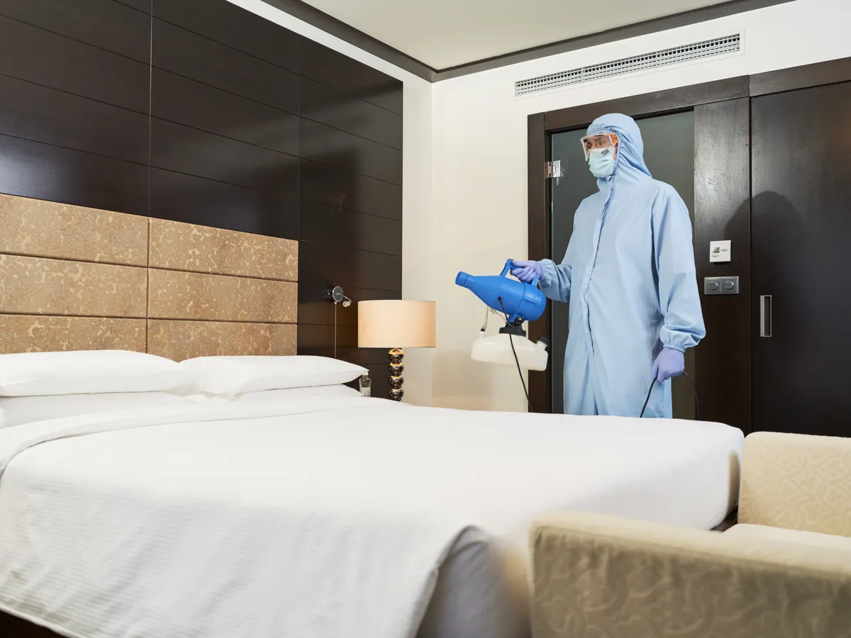 Technicien en combinaison de protection qui traite une chambre d'hôtel